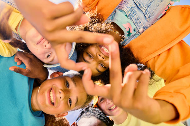 Elementary age children of diverse ethnicities playing together, forming a heart shape with their fingers, symbolizing unity and friendship