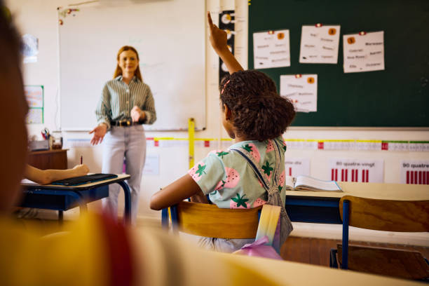 istock Elementary schoolgirl raising hand in classroom to answer teacher's question 2189309925