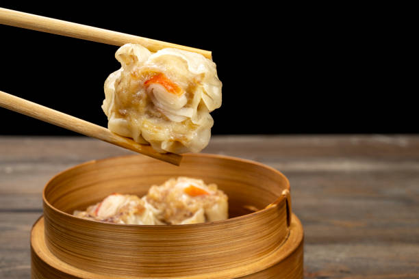 istock Human hand with chopstick eating chinese dim sum dumpling on bamboo wooden basket bowl on wooden table 2189309979