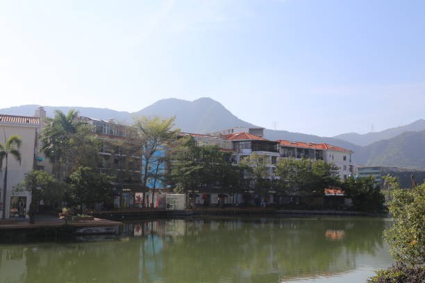 A river runs through a town with a view of mountains in the background. The buildings are tall and white, and there are palm trees lining the river. The scene is peaceful and serene
