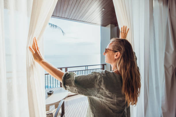 istock Woman Opening Curtains to Balcony with Ocean View 2189314020