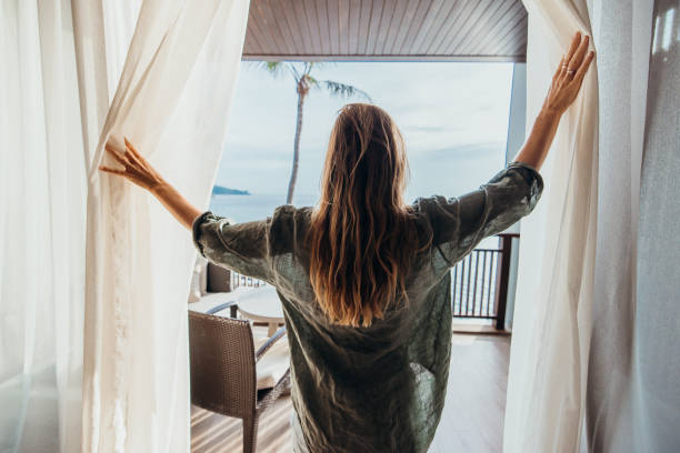 Woman Opening Curtains to Balcony with Ocean View
