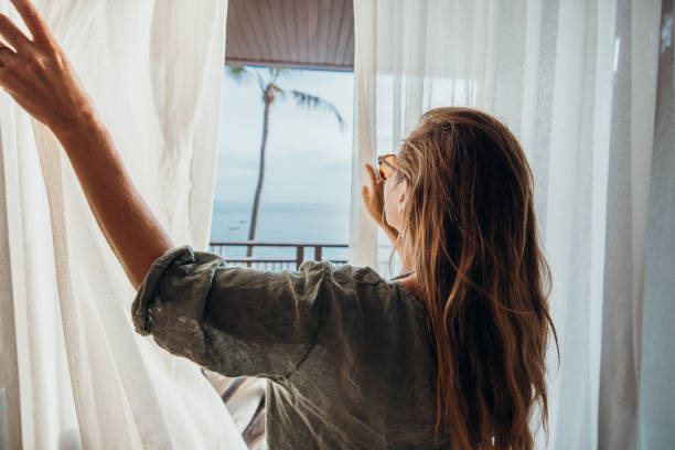 istock Woman Opening Curtains to Balcony with Ocean View 2189314090