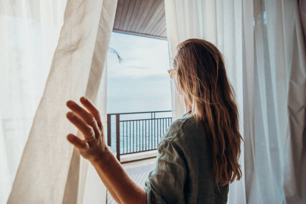 istock Woman Opening Curtains to Balcony with Ocean View 2189314143