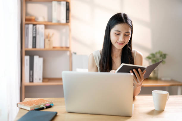 istock Beautiful young Asian woman working with laptop computer in home, reading book. 2189322292