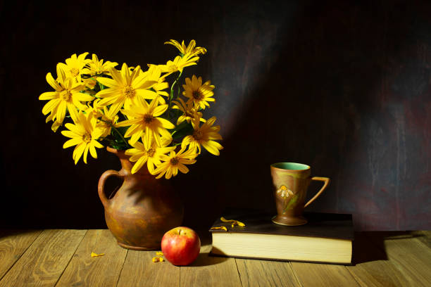 istock Still life, yellow flowers in a ceramic vase, apple, book and teacup 2189323032