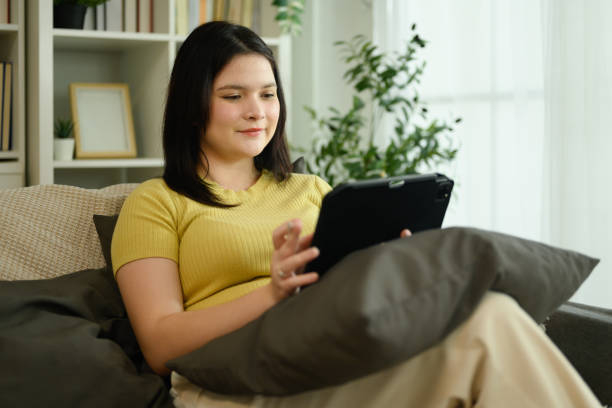 istock Cute curvy woman using digital tablet on sofa in bright living room 2189324975