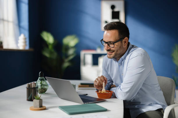 istock Happy businessman eating his lunch while working on laptop in the office. 2189327595