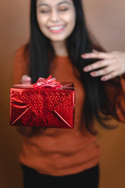 portrait of beautiful, happy indian young woman showing and holding red gift box.