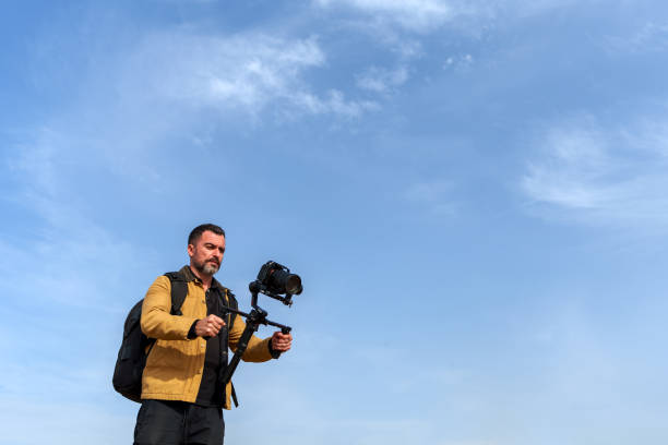 istock Mid adult videographer recording with professional camera and gimbal stabilizer against blue sky 2189335152