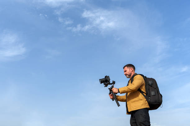 istock Videographer using a gimbal and camera to capture vibrant outdoor scenes under a blue sky with fluffy clouds 2189335156