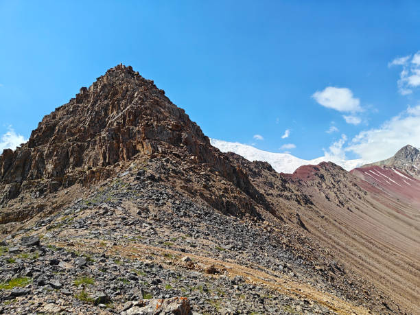 istock A rugged mountain peak rises above rocky terrain under a blue sky with clouds and a snow-capped summit 2189335242