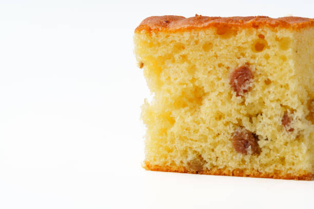 A slice of moist cake featuring raisins is showcased on a clean, white background, highlighting its soft texture and inviting appearance during a home baking activity.