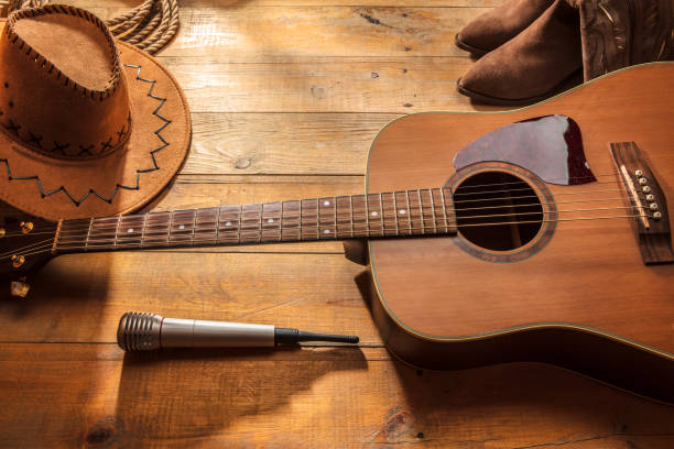 Acoustic guitar, microphone, lasso, cowboy hat and boots on a barn wood texture background. American Country music concept.