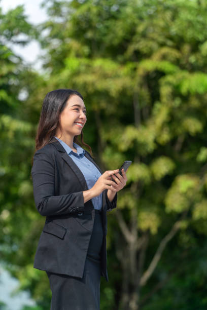 istock Asian Businesswoman Using Smartphone Outdoors with Lush Green Background 2189346728