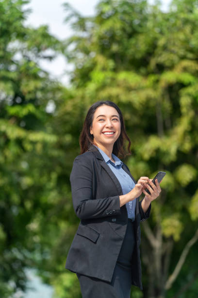 istock Asian Businesswoman Using Smartphone Outdoors with Lush Green Background 2189346735