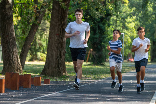 istock Trainer runs alongside two boys in a sunny park, focusing on improving their endurance and physical fitness. The boys are energized, learning proper running techniques while enjoying outdoor exercise 2189348403