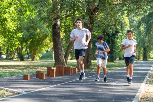 istock Trainer runs alongside two boys in a sunny park, focusing on improving their endurance and physical fitness. The boys are energized, learning proper running techniques while enjoying outdoor exercise 2189348503