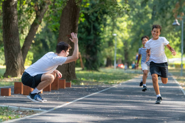 istock Trainer runs alongside two boys in a sunny park, focusing on improving their endurance and physical fitness. The boys are energized, learning proper running techniques while enjoying outdoor exercise 2189348857