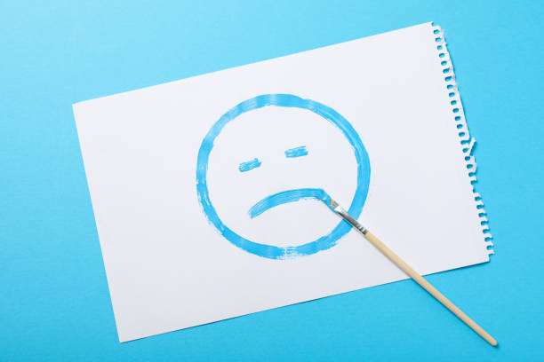 White paper with sad emoji and brush on blue background, top view