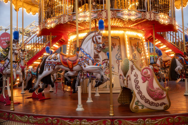 Carousel horses with colorful saddles and blue plumes gallop on a vintage carousel illuminated at dusk, creating a magical amusement park atmosphere