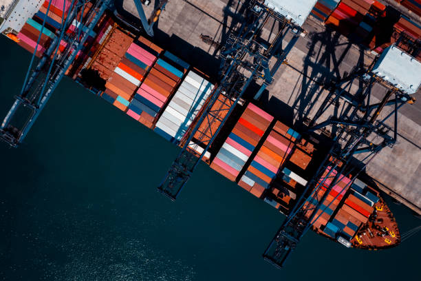 istock commercial port in deep sea load and unloading cargo from container ship import export by crane for distributing goods by trailers transport logistic  to customers and dealers, aerial top view 2189360752