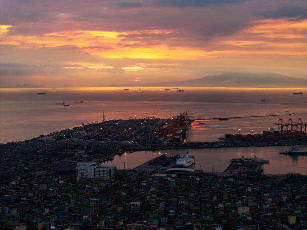 istock Manila's lively port area at sunset, featuring cargo ships dotted across the horizon against a dramatic sky with colorful clouds, and city lights twinkling below 2189363085