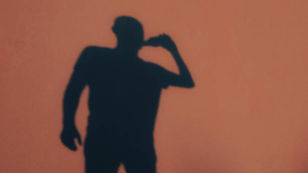 istock Shadow figure. A man drinks alcohol from a bottle. Back view of shadow. Alcohol Abuse 2189366470