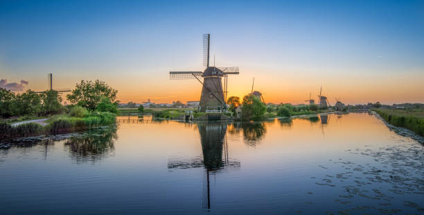 istock Windmills reflect in calm water during sunset in a serene countryside landscape 2189370549
