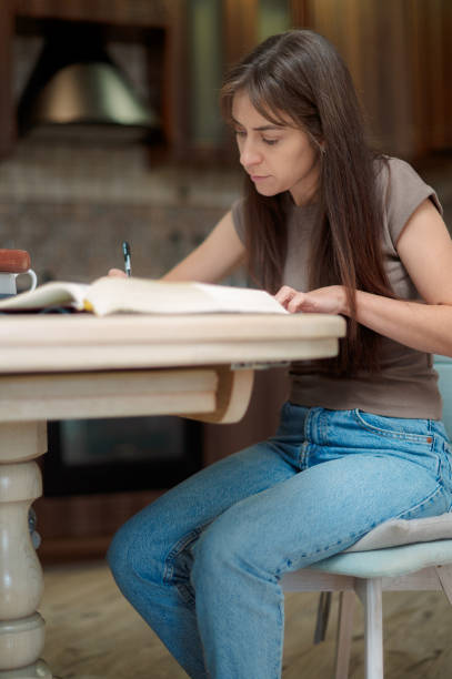 istock Focused female student learning and preparing exam at home, reading textbook and taking notes 2189370760