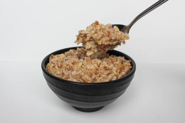 istock Cooked plain rolled oat inside black bowl and one silver spoon, Isolated on white background 2189373803