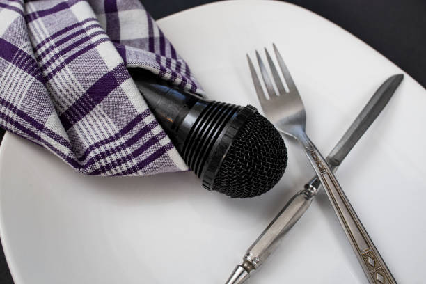 istock Black microphone wrapped in a purple napkin next to fork and knife on a white plate, culinary blog creative concept 2189375493