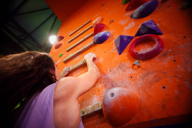 Young brunette male with long black hair works during climbing sessions on vertical walls in a sport climbing gym