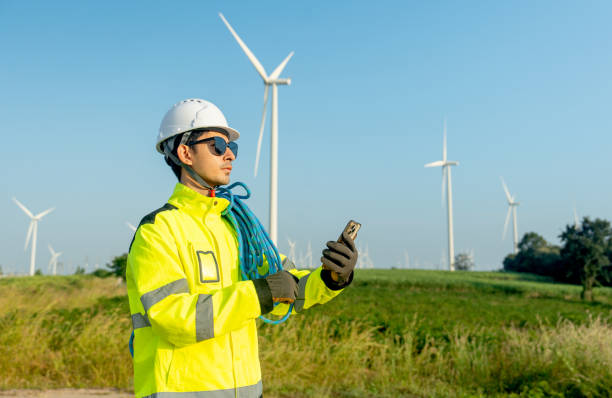 istock Side view wind turbine or windmill engineer worker hold mobile phone and look forward with row of wind turbine in the background. 2189377394