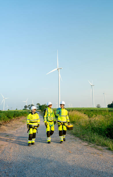 istock Vertical image of wind turbine or windmill workers or technicians talk  to discuss work and walk along the road in workplace field with row of wind turbine in the background. 2189377524
