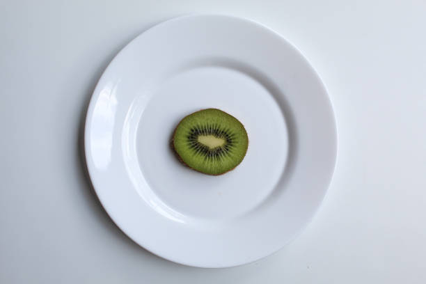 One slice of kiwi fruit, on white plate, isolated on white background, flat lay or top view
