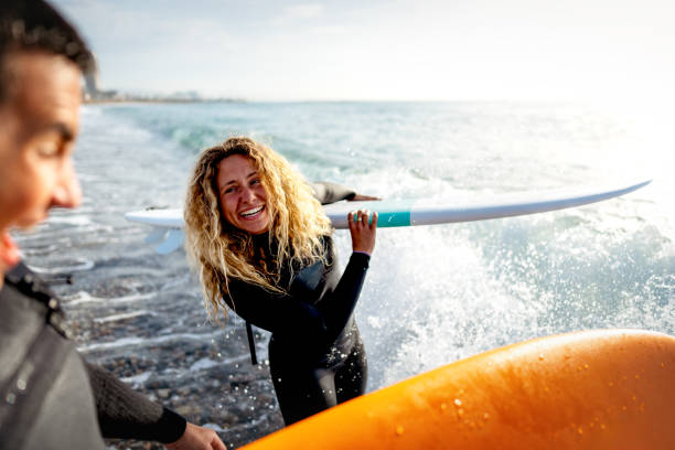 istock Beautiful happy surfer couple having fun on the beach, running with surfboard to the waves 2189380708