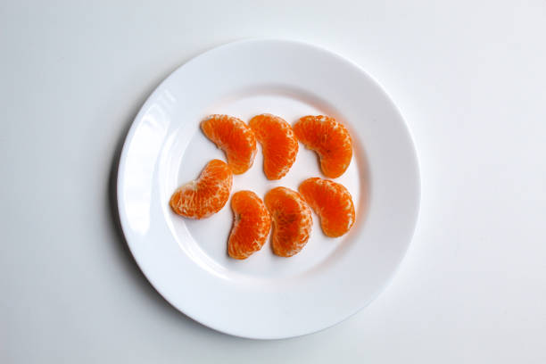 Some orange fruit segments, on white plate, isolated on white background, flat lay or top view