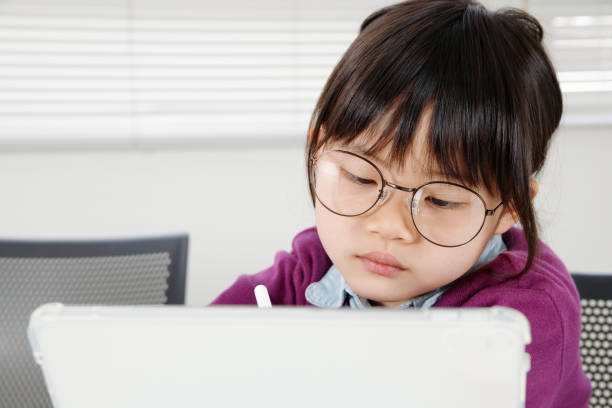 An elementary school girl with glasses operating a tablet and studying