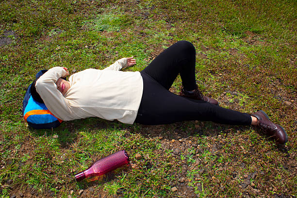 Tired Female Hiker lies on a Grassy Field, her Backpack and Water Bottle Placed Beside her Under the Bright Sun. She Takes a Moment to Recover From her Journey. This Peaceful Scene Reflects the Effort and Tranquility of Outdoor Exploration.