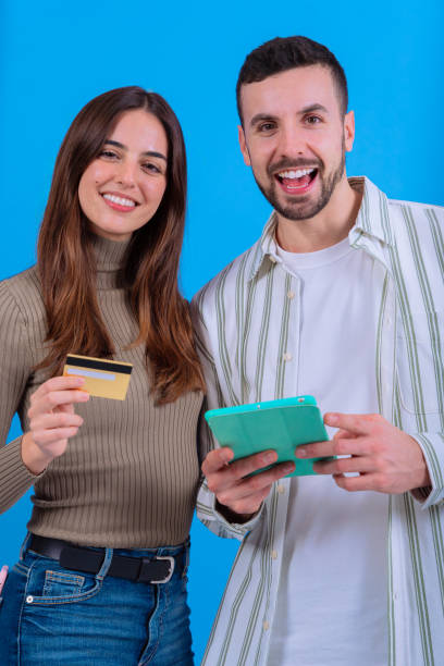 istock Happy couple holding a credit card and tablet against a blue background.Vertical 2189389321