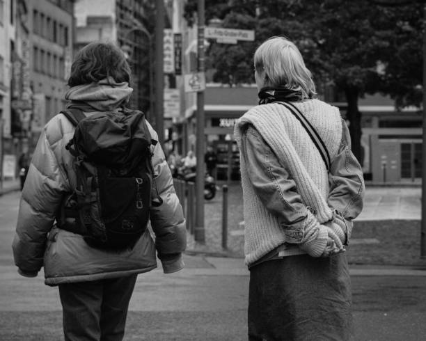 Cologne, Germany - October 27, 2023: Two friends walk side by side through the streets of Cologne, bundled up in winter clothes. Their backs turned to the camera create a sense of simplicity and companionship. Around them, the urban atmosphere shines with buildings and typical street signs of the city.