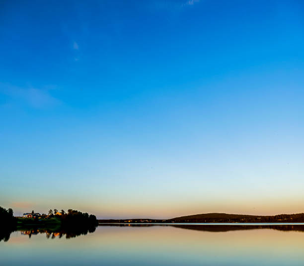 A beautiful blue sky with a calm lake in the foreground. The sky is clear and the sun is setting, creating a serene and peaceful atmosphere