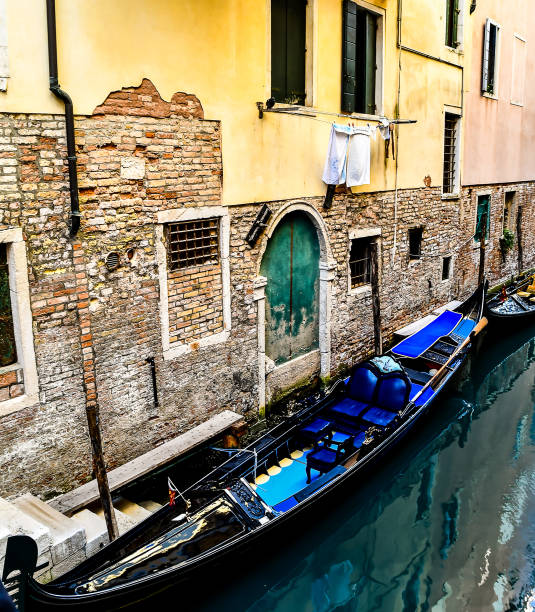 A blue boat is sitting in a canal next to a building. The boat is tied to a dock and has a blue seat. The scene is peaceful and serene, with the water reflecting the surrounding buildings