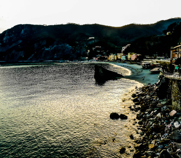 A beach with a boat in the water and a rocky shore. The water is calm and the sky is a beautiful orange color