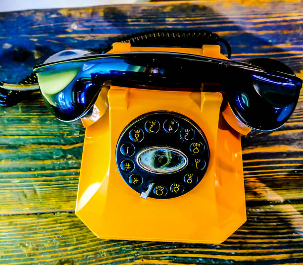 A yellow phone with a black dial sits on a wooden table. The phone is old and has a vintage look to it