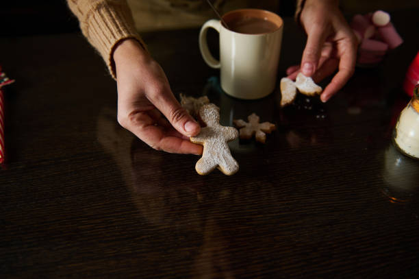 Hands holding gingerbread cookies on a table with hot chocolate, evoking warm holiday vibes.