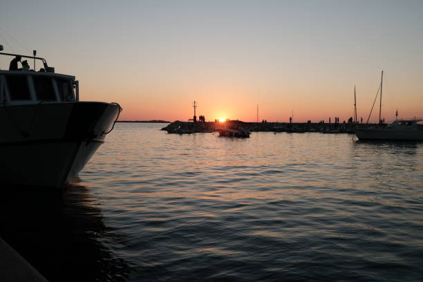 Boat at harbour in the foreground. People walking by the harbour dock with sunset in the background.