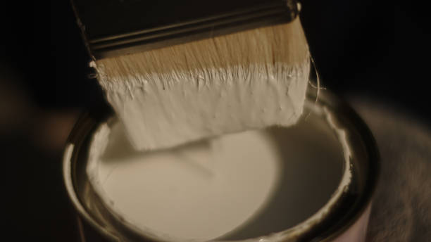 Dipping a brush into a bucket with white paint.
