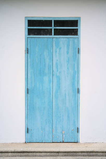 Blue old and deteriorated door with glass lighting window in the white concrete wall